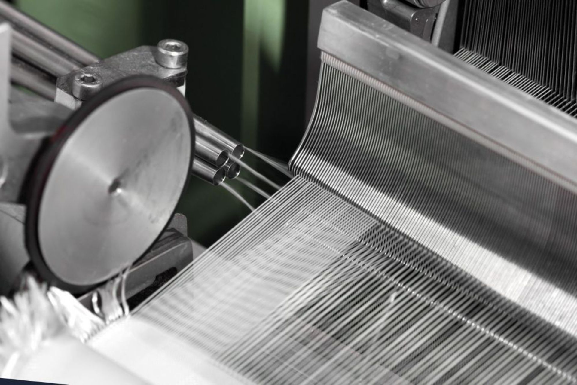 Nahaufnahme einer Webmaschine. Man sieht, wie Metallkomponenten und Fäden zu Stoff verwoben werden.